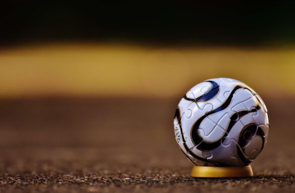 Piłka do futbolu leżąca na murawie, w półmroku. Tło jest zamazane.