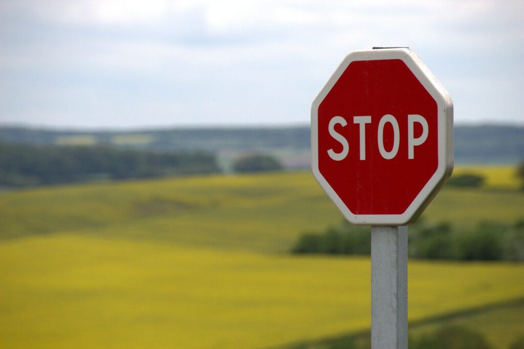 Czerwony znak Stop w tle wiosennego, rolniczego pejzażu przy lekko zachmurzonym niebie.